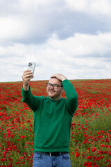 A cheerful Caucasian man capturing a selfie amid fiery poppy fields during Poppy Day, embracing...