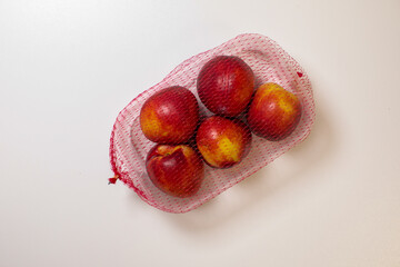 Ruby-hued nectarines cradled in netted pouch, evoking Sunburn Festival's zest, solstice harvest, and rustic fruit tapestry