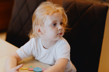 An adorable 3-year-old girl plays with building blocks and board games, capturing pure childhood...