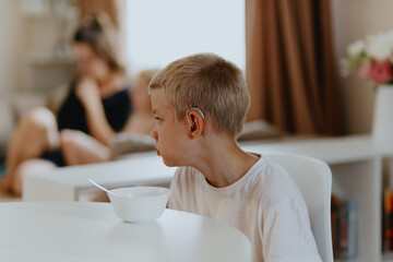 A boy with hearing aids enjoys a healthy breakfast, showcasing inclusive daily routines and...