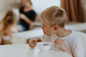 A boy with hearing aids enjoys a healthy breakfast, showcasing inclusive daily routines and...