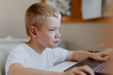 A boy with hearing aids enthusiastically plays computer games, showcasing inclusive play and...