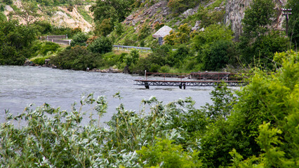 A tranquil pier juts into the murmuring river amidst verdant thickets, evoking serenity for World...