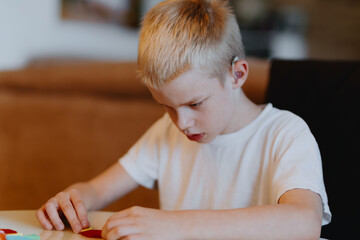 A boy with hearing aids focuses intently while playing with building blocks and board games,...