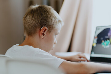 A boy with hearing aids enthusiastically plays computer games, showcasing inclusive play and...