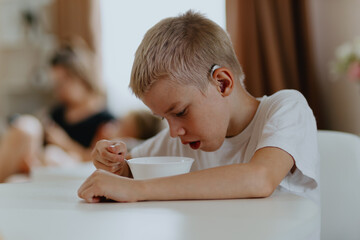 A boy with hearing aids enjoys a healthy breakfast, showcasing inclusive daily routines and...