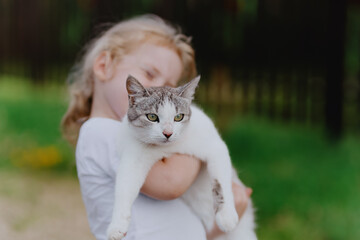 A sweet 3-year-old girl gently holds a cat, showcasing pure love between children and pets....