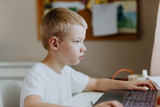 A boy with hearing aids enthusiastically plays computer games, showcasing inclusive play and childhood development. Perfect for disability awareness and modern education content