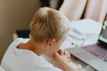 A boy with hearing aids enthusiastically plays computer games, showcasing inclusive play and...