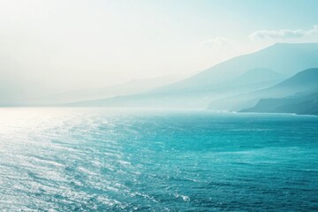 Turquoise ocean waves meet misty blue mountains under a hazy sky