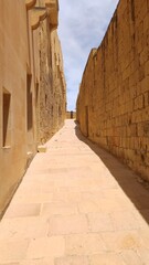 Sunny narrow stone alley with historic walls in Gozo, Malta. Traditional Mediterranean architecture and old limestone buildings, perfect for travel, tourism and history themes.
