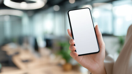 Fototapeta na wymiar Person holding a blank screen smartphone in an office environment with blurred background detail visible