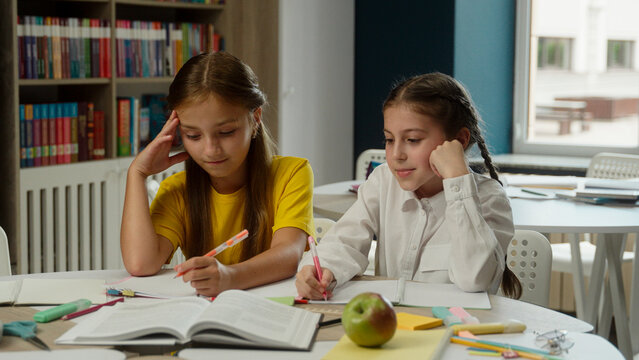 Caucasian little girls classmates kids teens schoolgirls pupils children school students class studying difficult task lesson learning writing homework together desk study primary education schoolwork