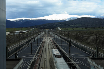 Fototapeta premium Train tracks and the snow-capped mountains of Sierra de Guadarrama in the background
