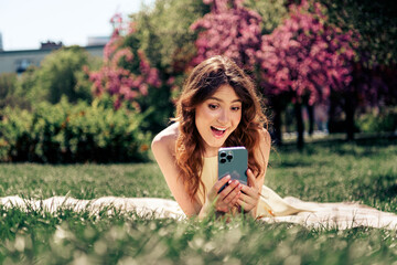 Lovely woman enjoying a sunny day outdoors, relaxing in the park with a phone, expressing happiness...