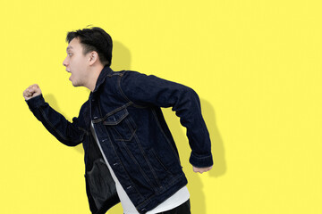 Joyful Asian Man in Denim Jacket running in yellow background