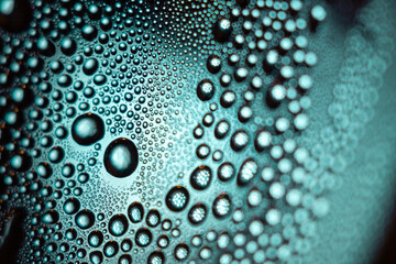 Blue abstract texture of transparent water drops on a glass surface, reflecting light like clear...