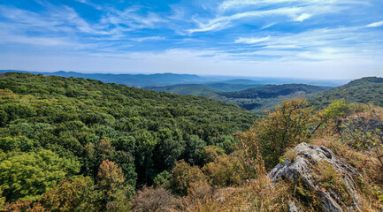 Looking southwest from Őr-kő, this scenic landscape in the Bükk Mountains captures early signs of autumn across the forested terrain. Rolling hills meet open sky, framed by ancient trees. 