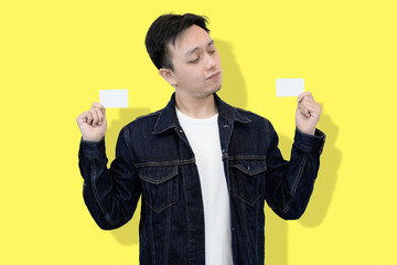 Young Man Holding Two Blank Cards, Yellow Background, Questioning Expression