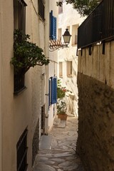 Fototapeta premium Empty narrow streets of Cadaqués, Spain, with white houses and clear blue sky. The peaceful historic town center is beautifully captured without any people, highlighting its charm and tranquility.