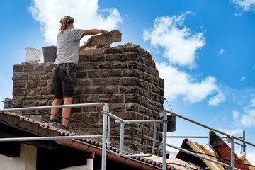 Roofer removes bricks by hand from a masonry chimney during renovation work