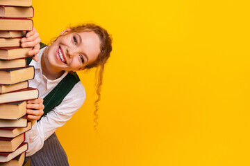 Cheerful girl peeking from a stack of books against a bright yellow background, symbolizing...