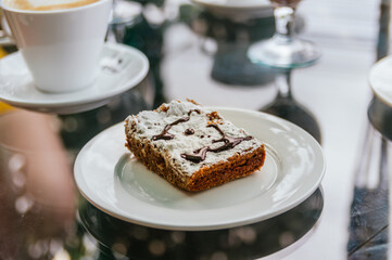 A brownie with white icing is sitting on a white plate