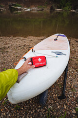 A person is seen holding a first aid kit while standing next to a paddleboard, indicating a...