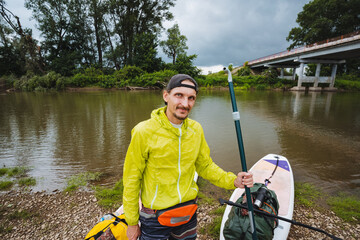 A man dressed in a bright yellow jacket stands alongside a beautiful blue river, fully prepared...