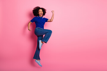 Cheerful young woman in trendy casual attire jumping with excitement against a vibrant pink...