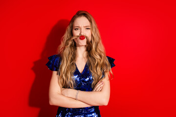 Naklejka premium Charming Woman in Shiny Blue Dress Posing With Playful Expression Against Vibrant Red Background
