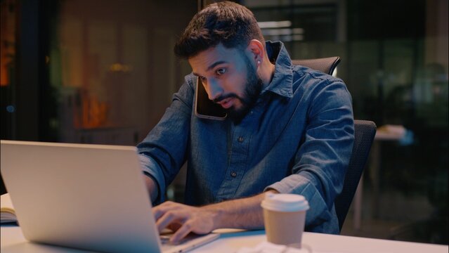 Businessman Indian guy multitasking business man male in night late office overtime work talking mobile phone call discuss computer laptop commerce smartphone conversation smiling manager consulting - Powered by Adobe