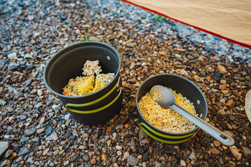 On a rugged, rocky surface, there are two bowls filled with food alongside a spoon placed...
