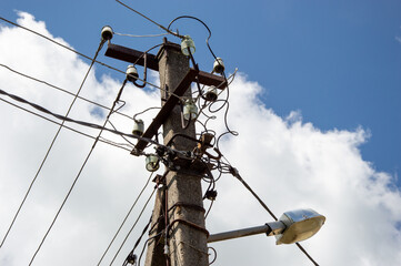 An electric utility pole stands tall against a bright blue sky, featuring numerous wires and...