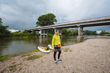 An avid adventurer is seen enjoying their time paddleboarding under a beautiful bridge that spans a...