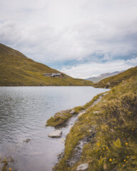 Mountain lake with hiking trail and alpine refuge under a moody sky in summer landscape