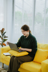 Young beautiful Asian woman in green shirt sitting using laptop in bright white office.