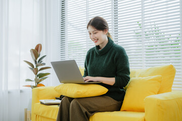 Young beautiful Asian woman in green shirt sitting using laptop in bright white office.