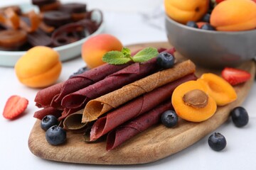 Tasty candied leather rolls, fruits and berries on white table, closeup