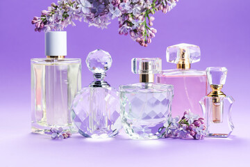 Bottles with perfumes and lilac flowers on purple gradient background, closeup