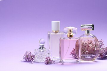 Bottles with perfumes and lilac flowers on purple gradient background, closeup. Space for text