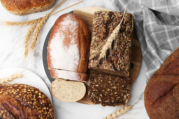 Freshly baked loaves of bread and spikes on white marble table, flat lay