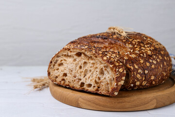 Freshly baked loaf of bread with oat flakes and spikes on light table against grey background,...