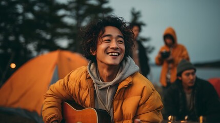 Young man playing guitar and smiling at campsite with friends