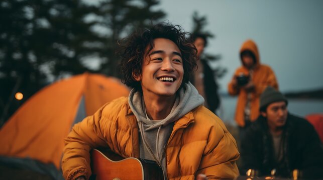 Young man playing guitar and smiling at campsite with friends