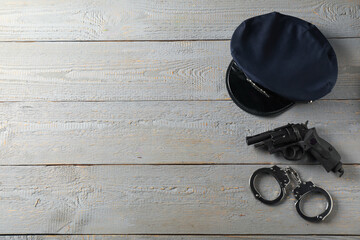 Police cap, gun and handcuffs on grey wooden table, flat lay. Space for text