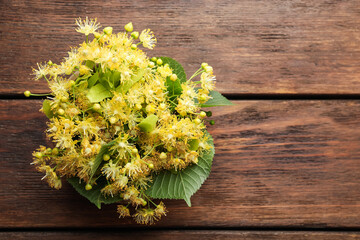 Beautiful linden flowers and green leaves on wooden table, top view. Space for text