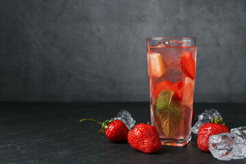 Refreshing drink with strawberries and ice on dark textured table against grey background, closeup....