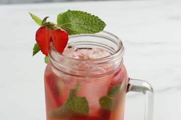 Refreshing drink with strawberries, ice and mint in mason jar on white table, closeup