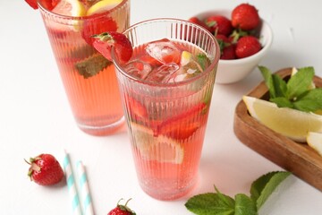 Refreshing drink with strawberries, mint, lemon and ice on white table, closeup